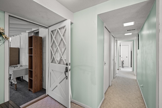 hallway featuring light carpet, a textured ceiling, visible vents, and baseboards