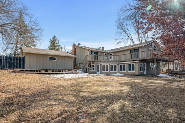 rear view of house featuring an outdoor structure, fence, a chimney, and a wooden deck