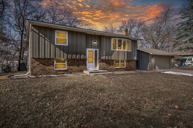 raised ranch with brick siding, a chimney, concrete driveway, an attached garage, and board and batten siding