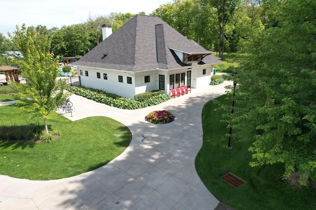 view of front facade with a shingled roof, a front yard, concrete driveway, and a chimney