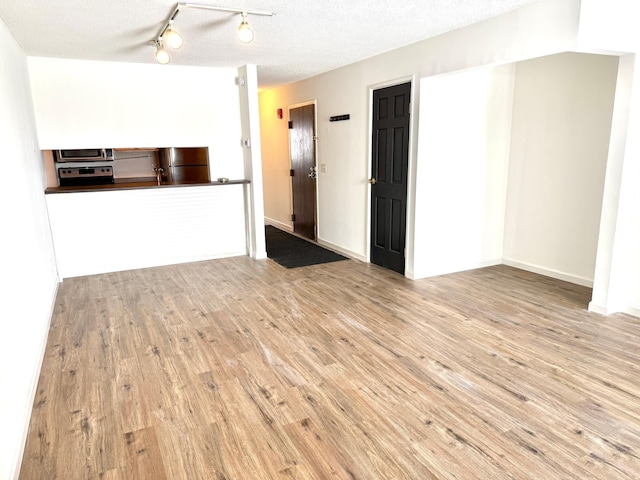 unfurnished living room featuring a textured ceiling, wood finished floors, and baseboards