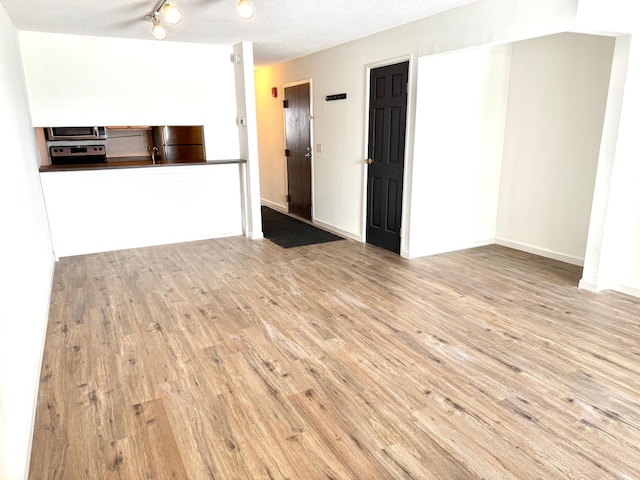 unfurnished living room with a textured ceiling, baseboards, and wood finished floors