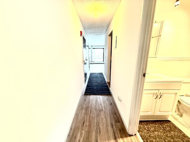 corridor with a textured ceiling, baseboards, and wood finished floors