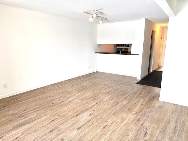 unfurnished living room with a textured ceiling, light wood-type flooring, and baseboards