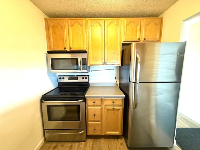 kitchen featuring baseboards, light wood-style flooring, stainless steel appliances, a textured ceiling, and light countertops