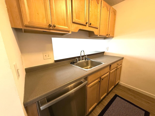 kitchen with baseboards, dark wood finished floors, dark countertops, stainless steel dishwasher, and a sink