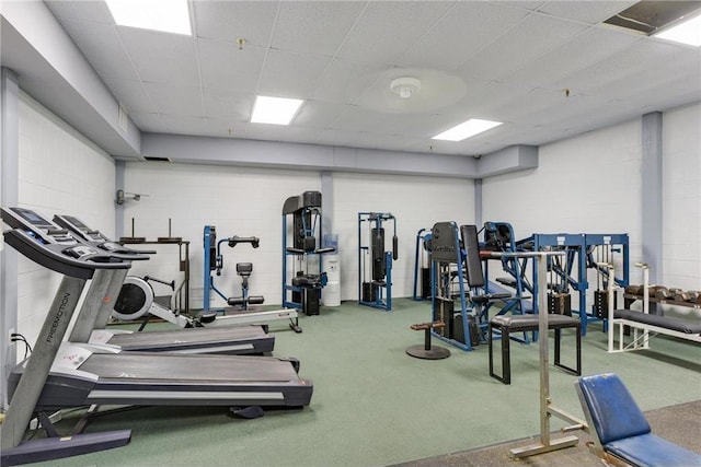 exercise room with a paneled ceiling and concrete block wall