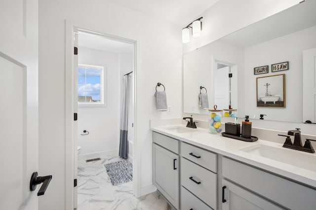 bathroom featuring double vanity, marble finish floor, toilet, and a sink