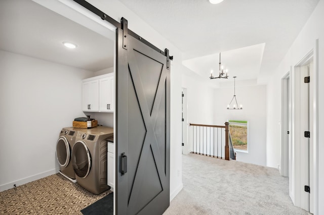 clothes washing area with a chandelier, a barn door, washing machine and dryer, light colored carpet, and cabinet space