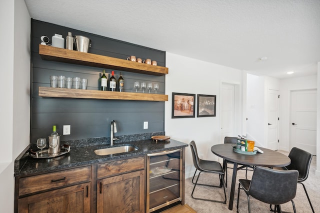 bar with a sink, a textured ceiling, wet bar, beverage cooler, and baseboards