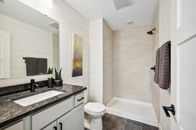 bathroom with toilet, vanity, a tile shower, and visible vents