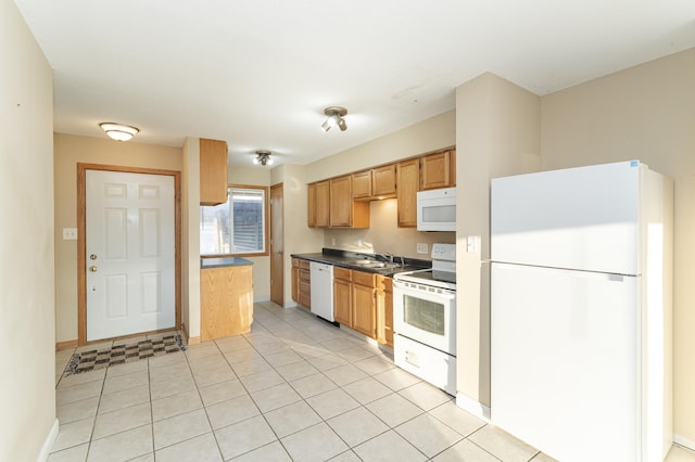 kitchen with dark countertops, baseboards, light tile patterned flooring, white appliances, and a sink