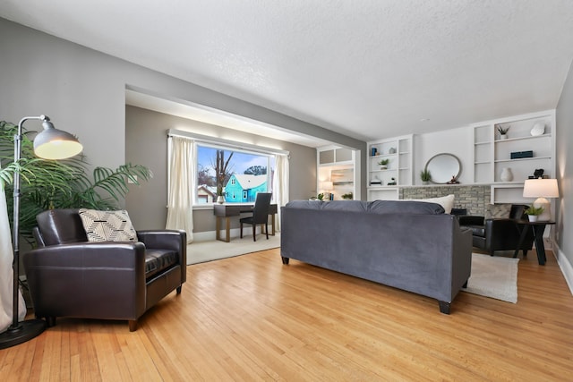 living area featuring baseboards, a textured ceiling, a brick fireplace, and light wood finished floors