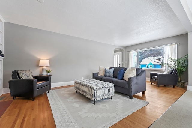 living area with arched walkways, light wood-style flooring, a textured ceiling, and baseboards