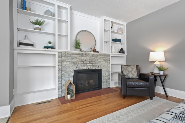 sitting room featuring visible vents, a brick fireplace, baseboards, and wood finished floors