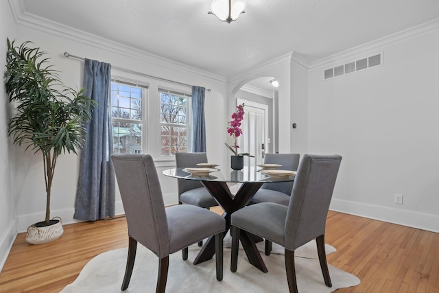 dining space featuring visible vents, crown molding, baseboards, light wood-style floors, and arched walkways