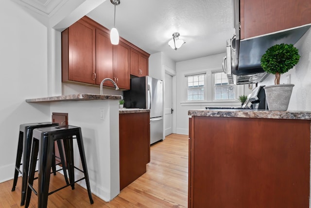 kitchen with light wood-style flooring, decorative light fixtures, freestanding refrigerator, a peninsula, and a breakfast bar area