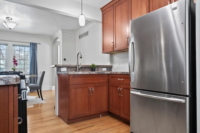 kitchen featuring dark stone counters, ornamental molding, freestanding refrigerator, light wood-style floors, and arched walkways