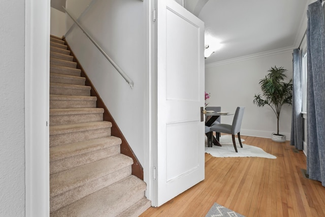 stairs with crown molding, wood finished floors, and baseboards