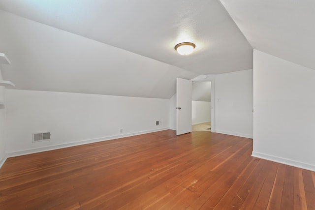 additional living space with vaulted ceiling, visible vents, baseboards, and hardwood / wood-style floors