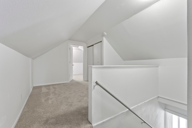 hall featuring baseboards, light colored carpet, an upstairs landing, and vaulted ceiling