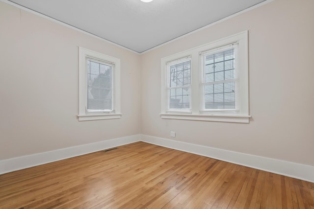 spare room with light wood finished floors, visible vents, baseboards, and ornamental molding