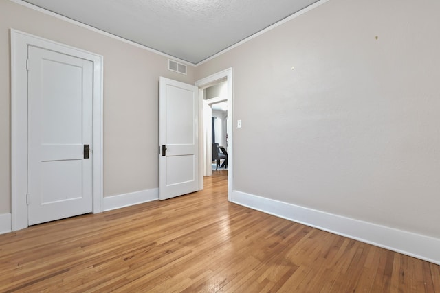 unfurnished bedroom featuring visible vents, baseboards, ornamental molding, and light wood finished floors