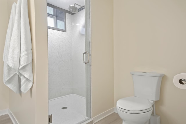 bathroom featuring a stall shower, toilet, baseboards, and wood finished floors