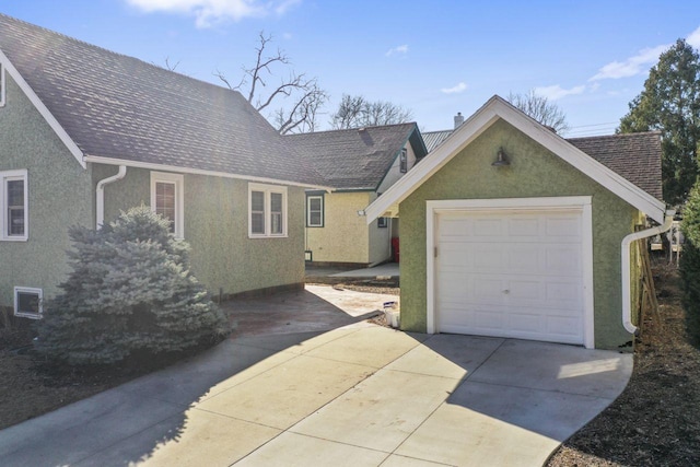 view of front facade featuring driveway, a shingled roof, a chimney, stucco siding, and a detached garage