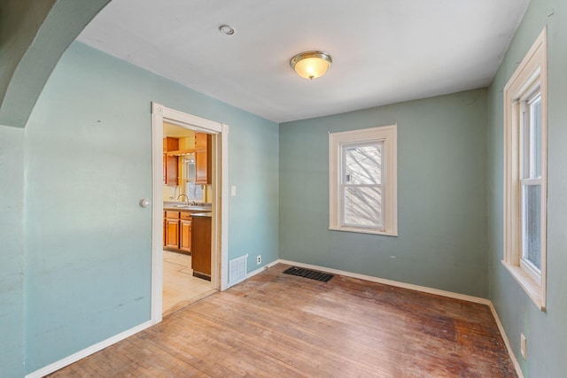 spare room with light wood finished floors, visible vents, baseboards, arched walkways, and a sink