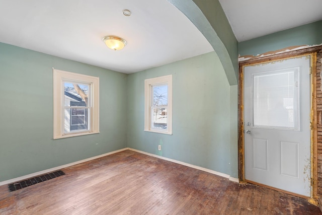 foyer with hardwood / wood-style flooring, arched walkways, visible vents, and baseboards