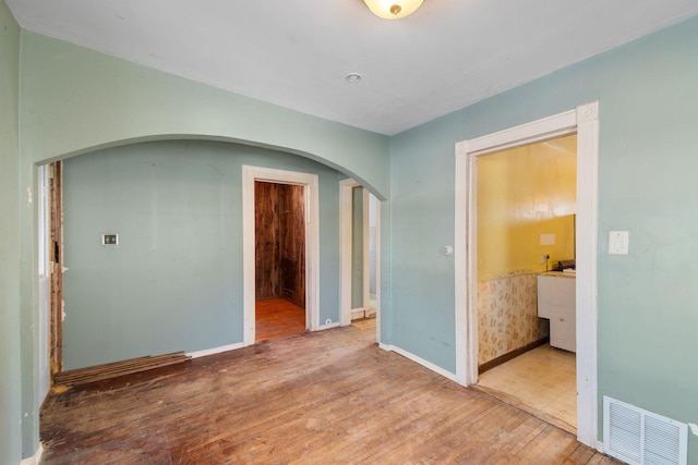 empty room with arched walkways, visible vents, wood-type flooring, and baseboards