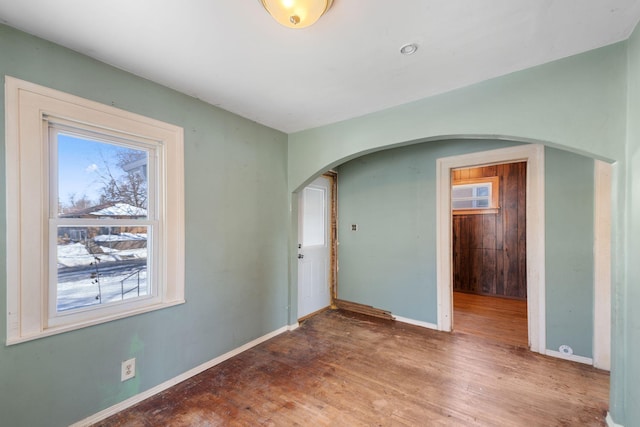 spare room featuring baseboards, arched walkways, and wood finished floors