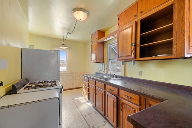 kitchen with gas range gas stove, light floors, brown cabinets, and a sink