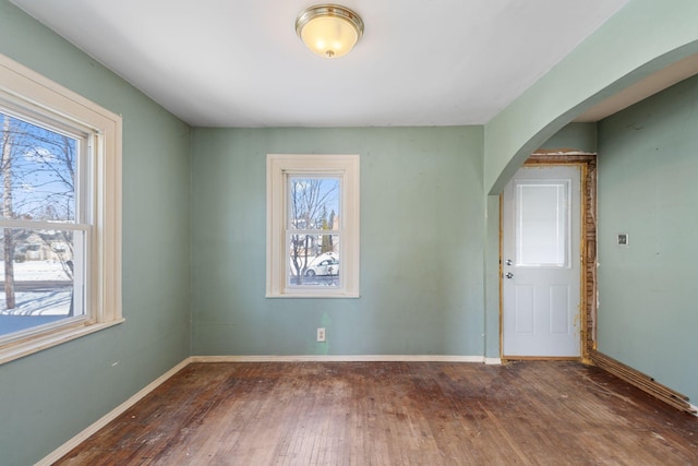 unfurnished room featuring baseboards, arched walkways, and wood-type flooring