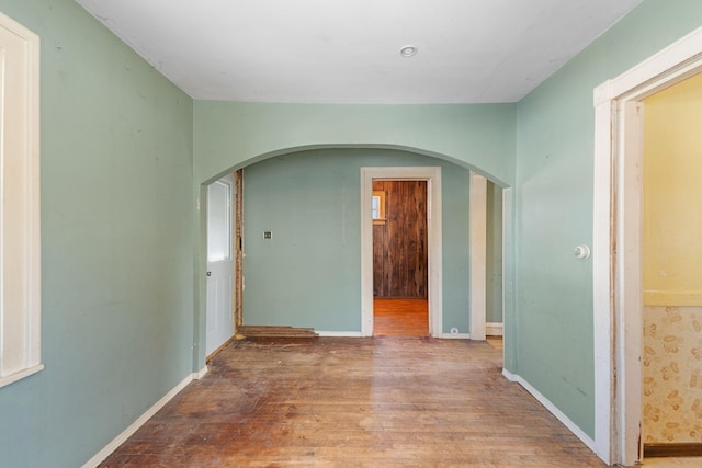 spare room with arched walkways, baseboards, and wood finished floors