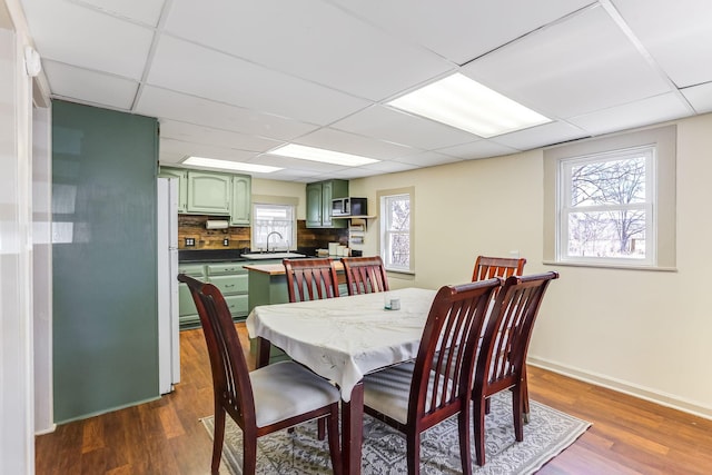 dining space featuring a drop ceiling, baseboards, and dark wood-style floors