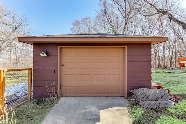 detached garage featuring concrete driveway and fence