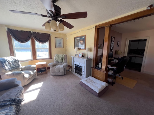 carpeted living room with a textured ceiling, ceiling fan, and a fireplace