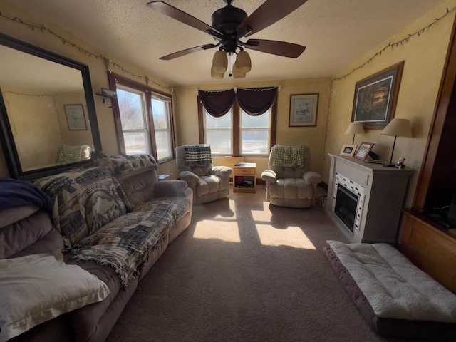 living room featuring a ceiling fan, a glass covered fireplace, carpet flooring, and a textured ceiling