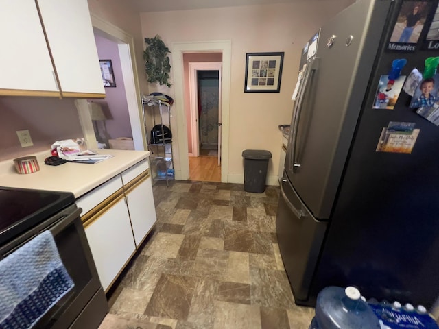 kitchen with light countertops, stove, freestanding refrigerator, stone finish flooring, and white cabinets