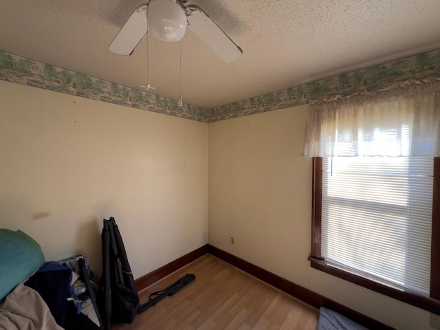 unfurnished room featuring a textured ceiling, ceiling fan, light wood-style flooring, and baseboards