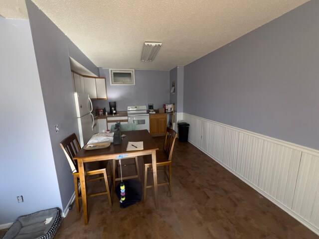 dining space featuring a textured ceiling and wainscoting