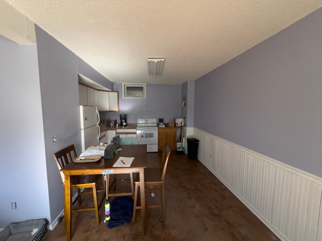 dining space featuring a textured ceiling and wainscoting