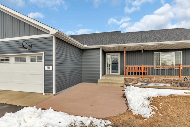 view of exterior entry with a garage and a shingled roof