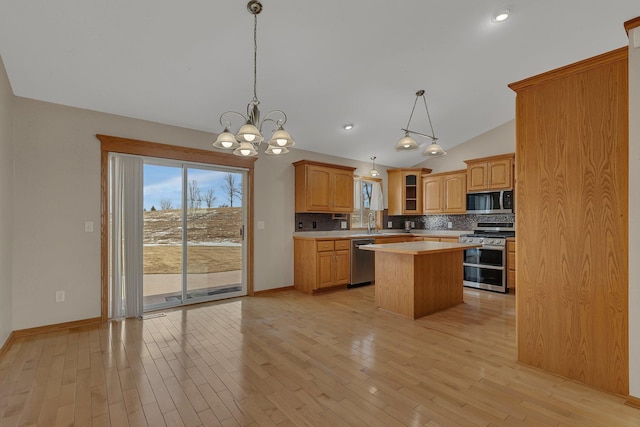 kitchen featuring light wood finished floors, a kitchen island, stainless steel appliances, light countertops, and backsplash