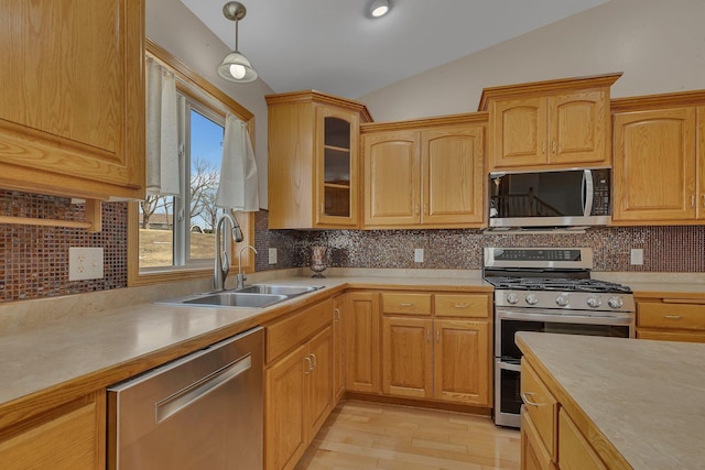 kitchen with appliances with stainless steel finishes, vaulted ceiling, a sink, and light countertops