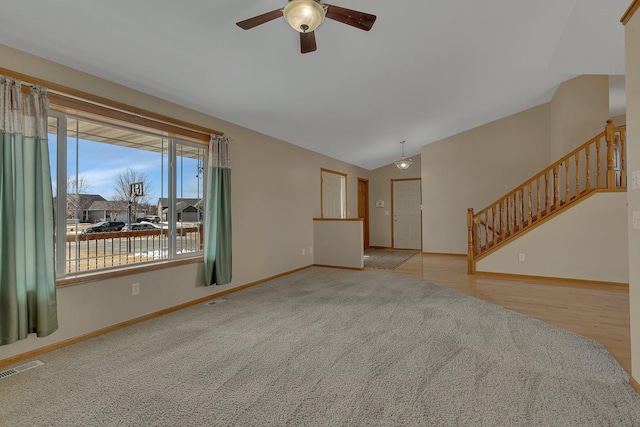 carpeted spare room featuring lofted ceiling, a ceiling fan, visible vents, baseboards, and stairway