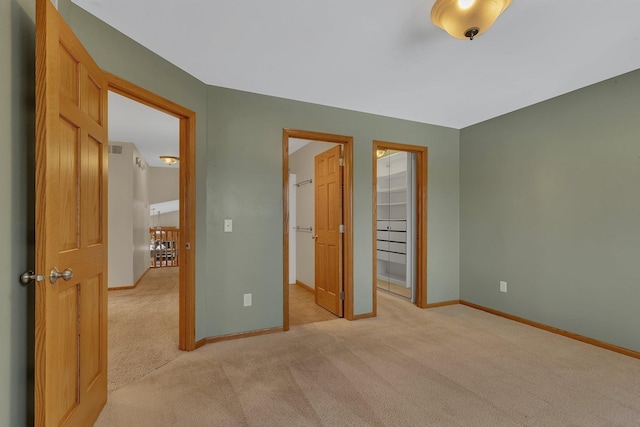 unfurnished bedroom featuring a walk in closet, a closet, visible vents, light carpet, and baseboards