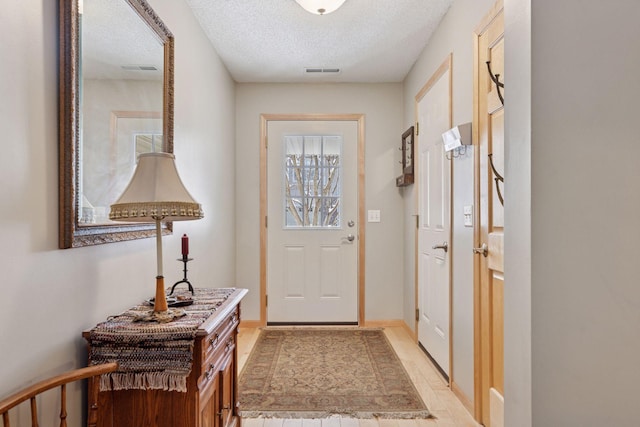 doorway to outside with a textured ceiling, visible vents, and baseboards